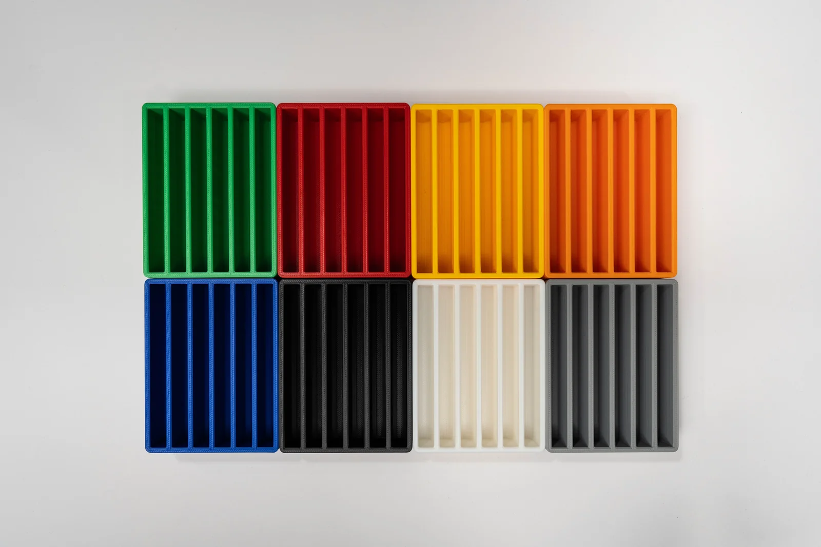 Eight 3D-printed SSD holders arranged in a four-by-two grid on white, in green, red, yellow, orange, blue, black, cream and gray.